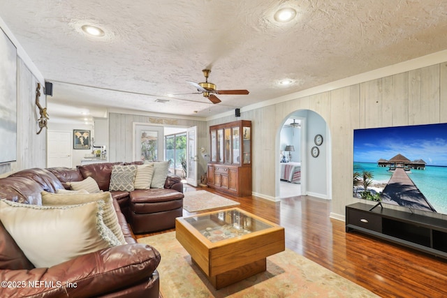 living area with ceiling fan, arched walkways, a textured ceiling, and wood finished floors