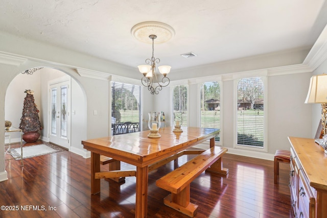 dining room featuring dark wood-type flooring, a notable chandelier, visible vents, and arched walkways