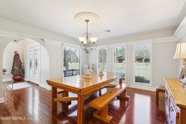 dining space with arched walkways, baseboards, dark wood-type flooring, and an inviting chandelier