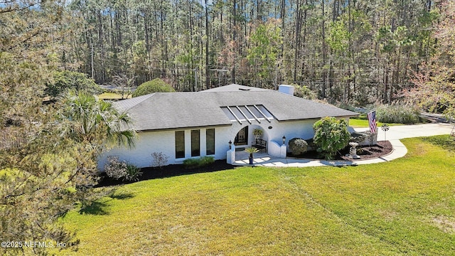 view of front of home featuring a wooded view, a shingled roof, and a front lawn