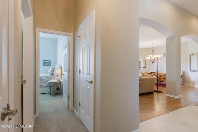 hallway with arched walkways, a chandelier, baseboards, and wood finished floors