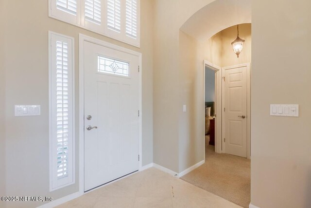 foyer with arched walkways, carpet, and baseboards