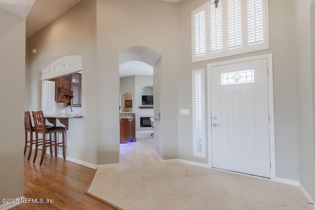 foyer entrance with light wood finished floors, baseboards, arched walkways, and a towering ceiling