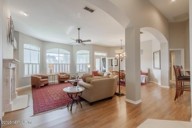 living area with visible vents, arched walkways, light wood finished floors, a premium fireplace, and baseboards