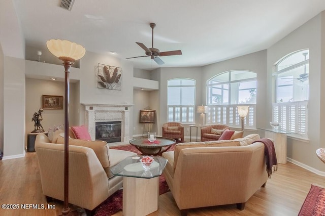 living room featuring light wood finished floors, visible vents, a fireplace, and a ceiling fan