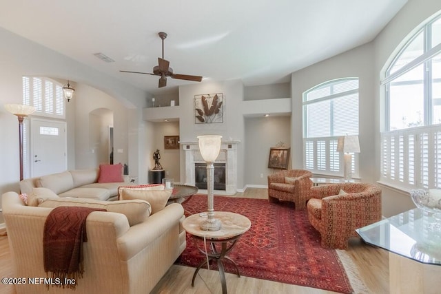 living room with a ceiling fan, visible vents, wood finished floors, a premium fireplace, and arched walkways