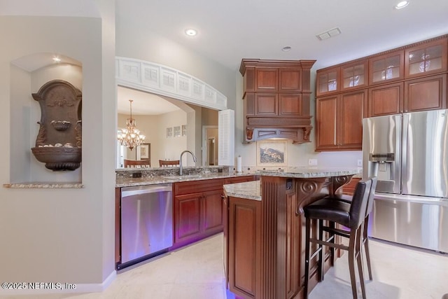 kitchen with visible vents, a kitchen breakfast bar, appliances with stainless steel finishes, glass insert cabinets, and light stone countertops