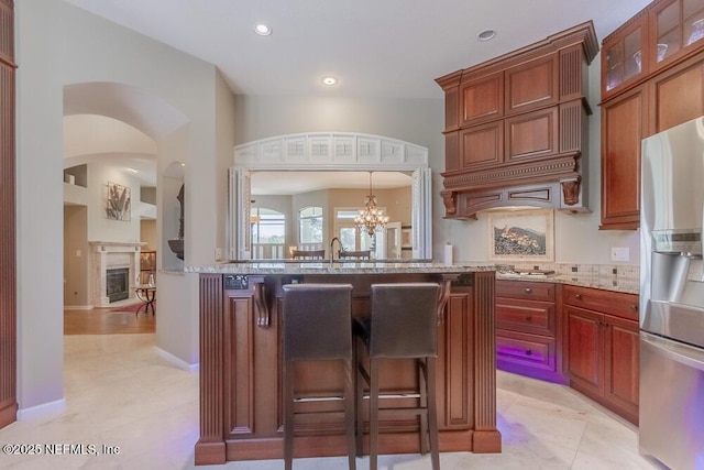 kitchen featuring a notable chandelier, light stone counters, a kitchen breakfast bar, stainless steel fridge, and glass insert cabinets