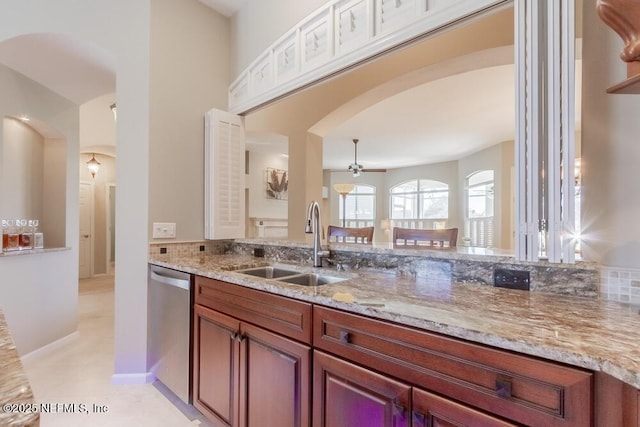 kitchen with ceiling fan, light stone counters, stainless steel dishwasher, arched walkways, and a sink