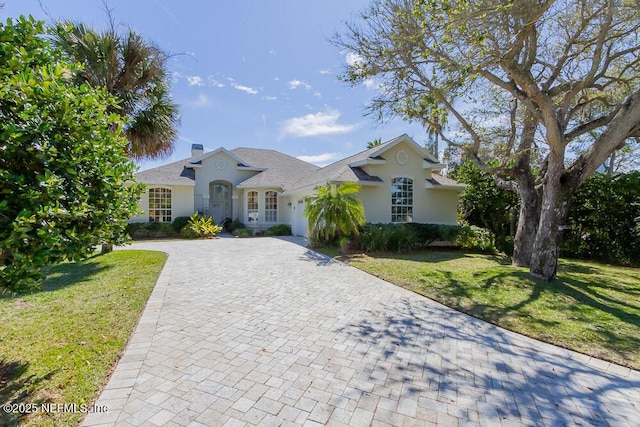 view of front of home featuring a front lawn, stucco siding, a chimney, decorative driveway, and an attached garage