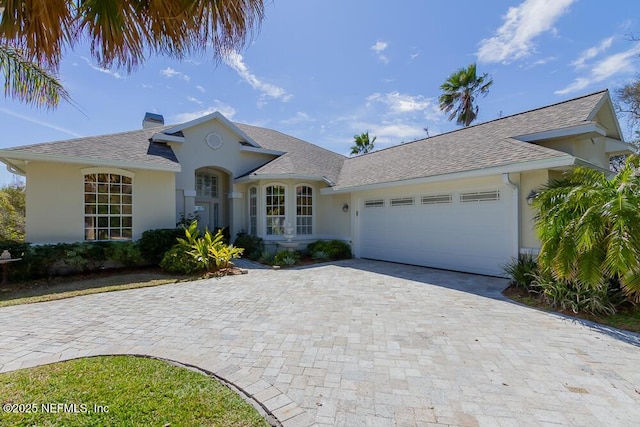 view of front of home with roof with shingles, an attached garage, a chimney, stucco siding, and decorative driveway