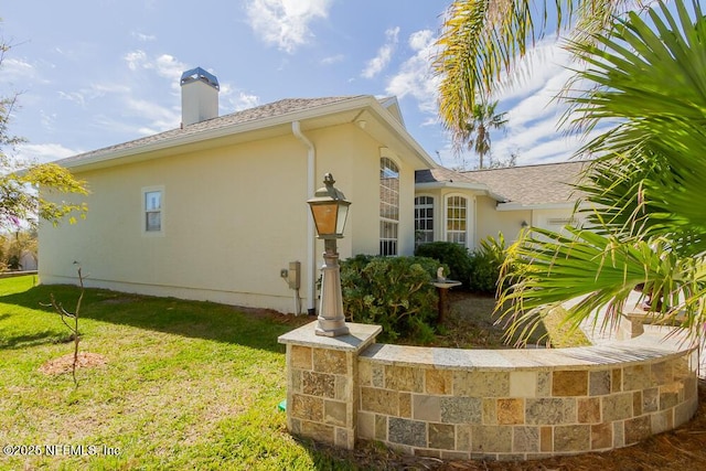 view of side of home featuring a chimney, stucco siding, and a lawn