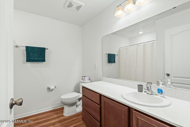 full bath with visible vents, toilet, wood finished floors, baseboards, and vanity