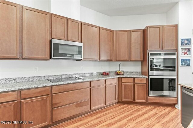 kitchen with light stone countertops, appliances with stainless steel finishes, brown cabinets, and light wood finished floors