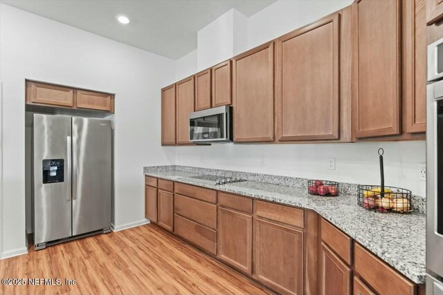 kitchen featuring light stone counters, light wood-style flooring, stainless steel appliances, and brown cabinets