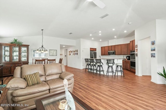 living area featuring visible vents, light wood-style flooring, ceiling fan with notable chandelier, recessed lighting, and lofted ceiling