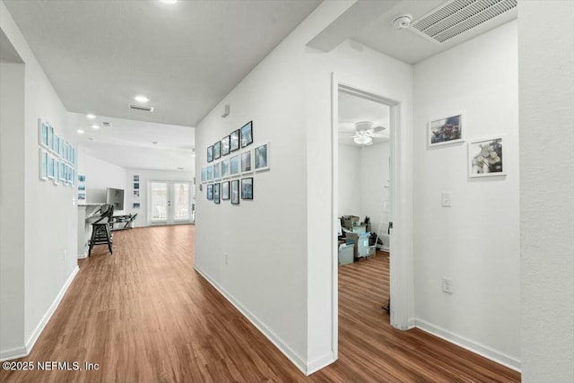 hall with wood finished floors, visible vents, and baseboards