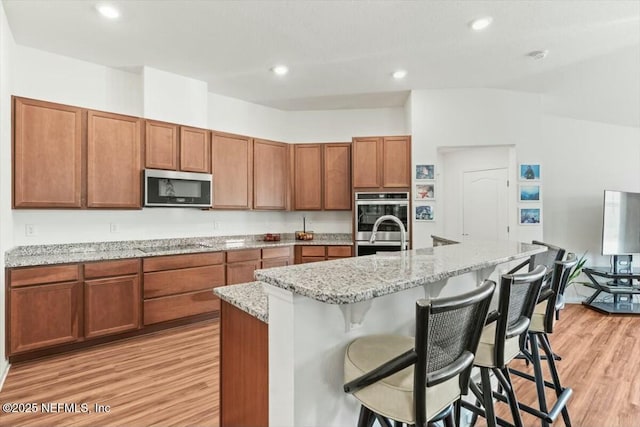 kitchen featuring brown cabinets, a kitchen island with sink, appliances with stainless steel finishes, a breakfast bar area, and light wood finished floors