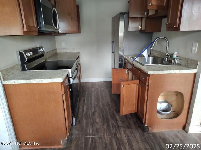 kitchen featuring brown cabinetry, dark wood finished floors, range with electric cooktop, a sink, and stainless steel microwave