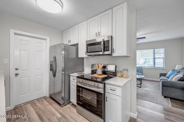 kitchen with stainless steel appliances, light countertops, white cabinets, light wood-style floors, and open floor plan