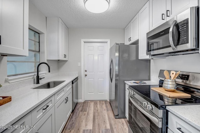 kitchen with a sink, light stone counters, white cabinetry, stainless steel appliances, and light wood finished floors