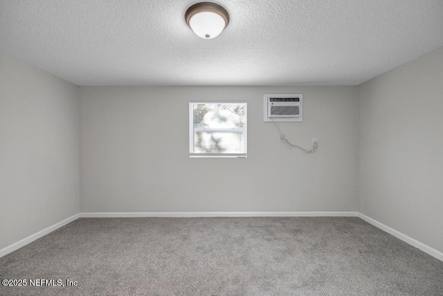 spare room with carpet flooring, a textured ceiling, a wall mounted AC, and baseboards