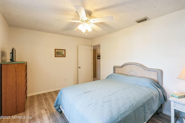 bedroom featuring visible vents, baseboards, a textured ceiling, and wood finished floors