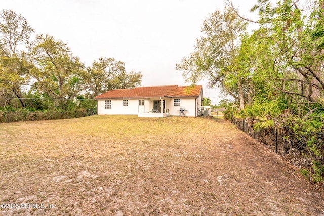 back of house featuring a tile roof, fence, a lawn, and stucco siding