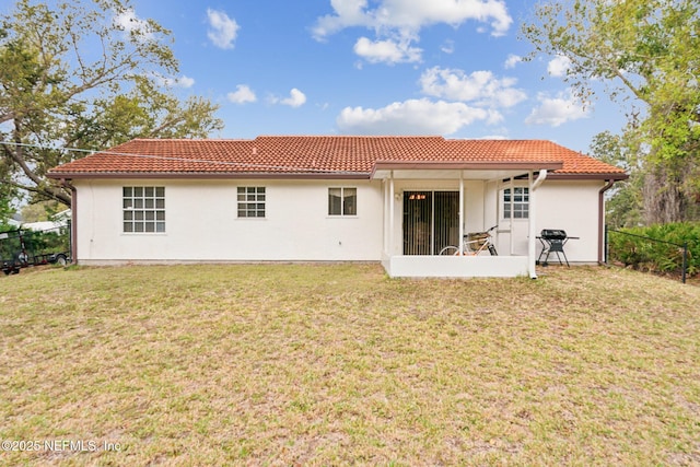 back of property with a tiled roof, a lawn, fence, and stucco siding