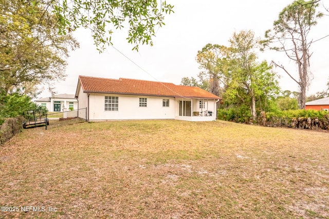 back of property featuring stucco siding, a tile roof, a yard, and fence