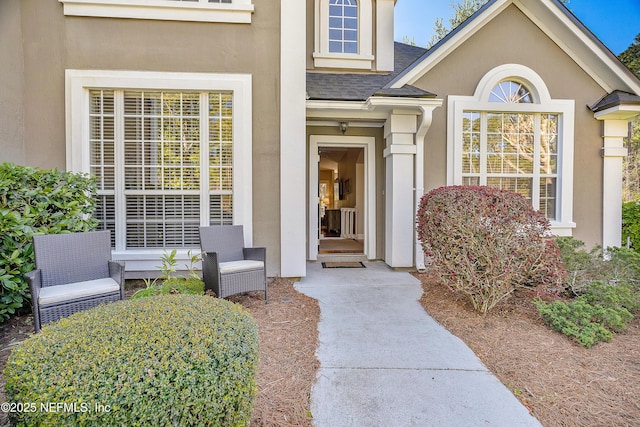 view of exterior entry featuring stucco siding and a shingled roof