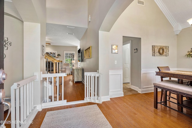 hall with arched walkways, visible vents, ornamental molding, and wood finished floors