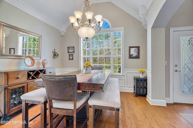 dining space with light wood-type flooring, a wainscoted wall, an inviting chandelier, crown molding, and lofted ceiling