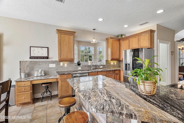 kitchen with visible vents, a sink, a kitchen breakfast bar, appliances with stainless steel finishes, and decorative backsplash