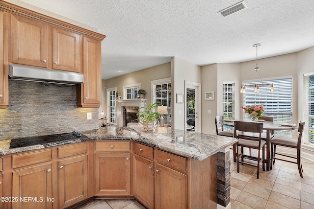 kitchen with black electric stovetop, visible vents, under cabinet range hood, and brown cabinets