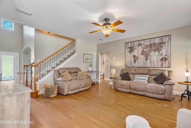 living room featuring visible vents, stairway, wood finished floors, arched walkways, and a textured ceiling