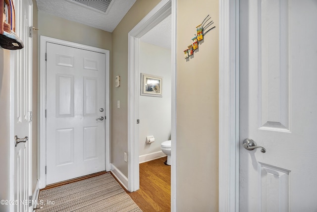 entrance foyer featuring light wood-type flooring, visible vents, baseboards, and a textured ceiling