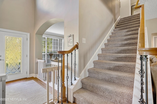 entryway featuring baseboards, arched walkways, wood finished floors, and stairs