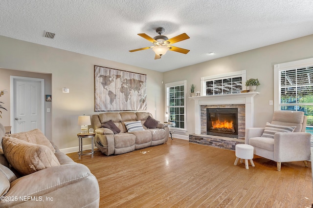 living area featuring wood finished floors, baseboards, visible vents, a fireplace, and ceiling fan