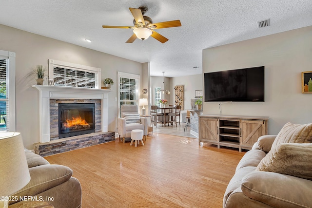 living area featuring wood finished floors, visible vents, a fireplace, ceiling fan, and a textured ceiling