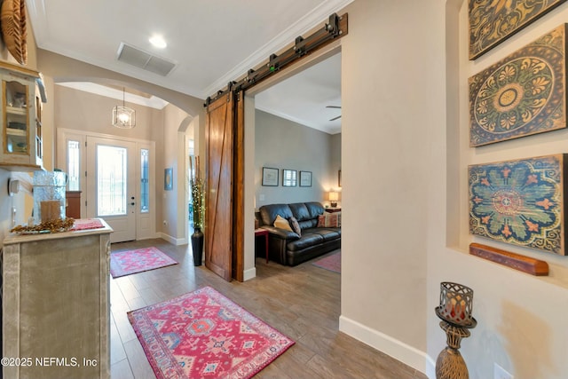 entrance foyer featuring arched walkways, crown molding, a barn door, and wood finished floors