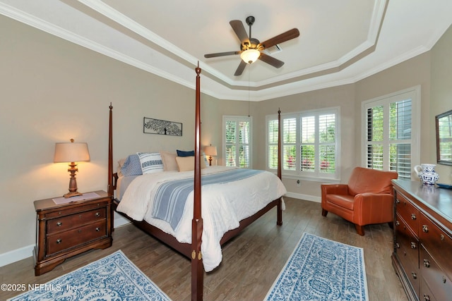 bedroom featuring baseboards, ornamental molding, wood finished floors, a raised ceiling, and a ceiling fan