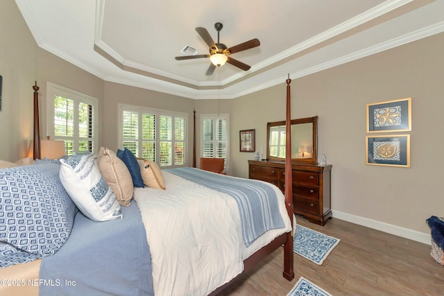 bedroom with visible vents, wood finished floors, baseboards, crown molding, and a raised ceiling