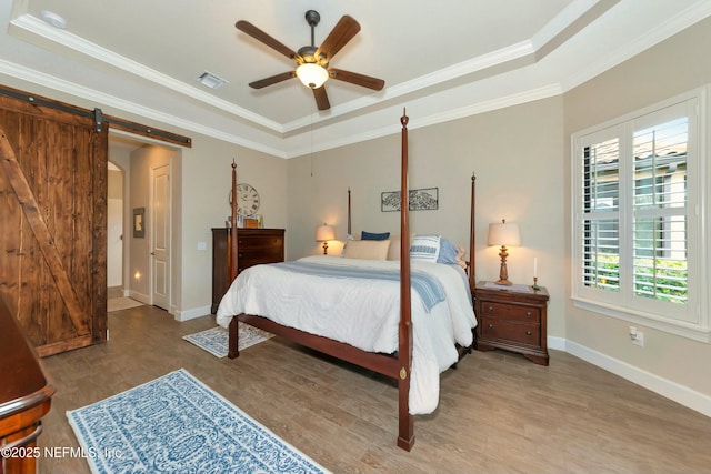 bedroom featuring a tray ceiling, visible vents, a barn door, and wood finished floors