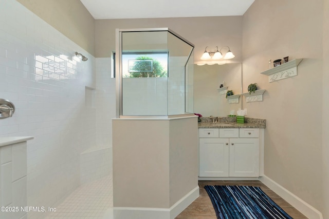 full bathroom with vanity, wood finished floors, a walk in shower, and baseboards