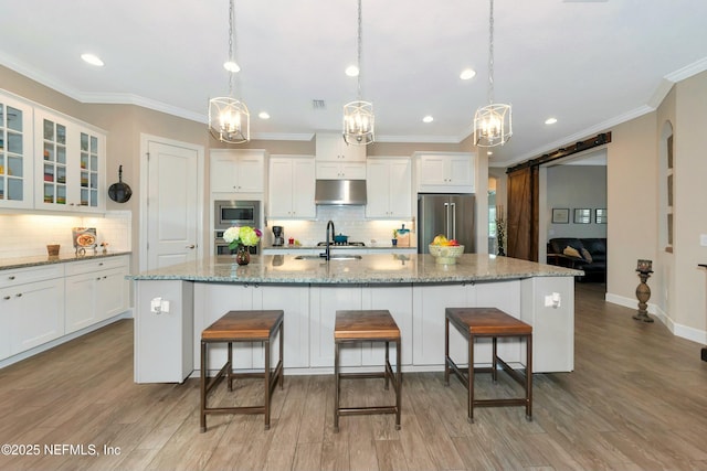 kitchen featuring a kitchen bar, under cabinet range hood, a sink, a barn door, and stainless steel appliances