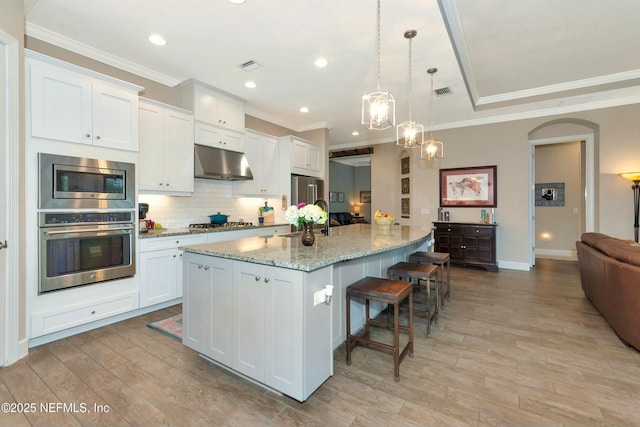 kitchen featuring under cabinet range hood, a sink, arched walkways, appliances with stainless steel finishes, and white cabinets