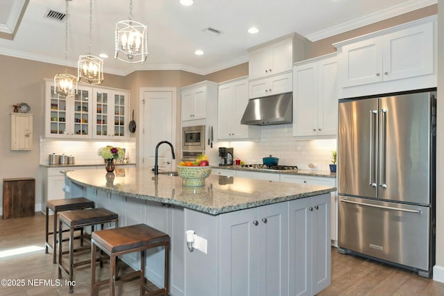 kitchen featuring light wood-type flooring, a kitchen bar, under cabinet range hood, appliances with stainless steel finishes, and white cabinets