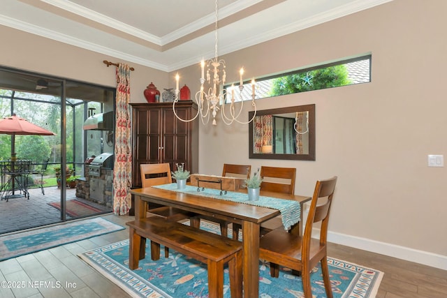 dining room featuring crown molding, baseboards, a tray ceiling, wood finished floors, and a notable chandelier