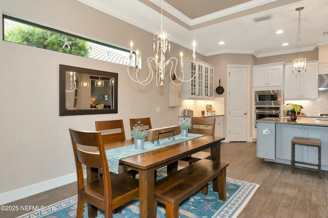 dining room featuring hardwood / wood-style floors, baseboards, visible vents, crown molding, and a notable chandelier